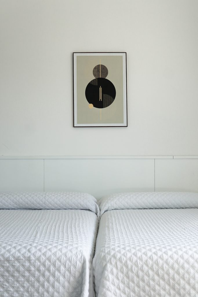 dos camas blancas con cuadro con circulos negro y marron en pared