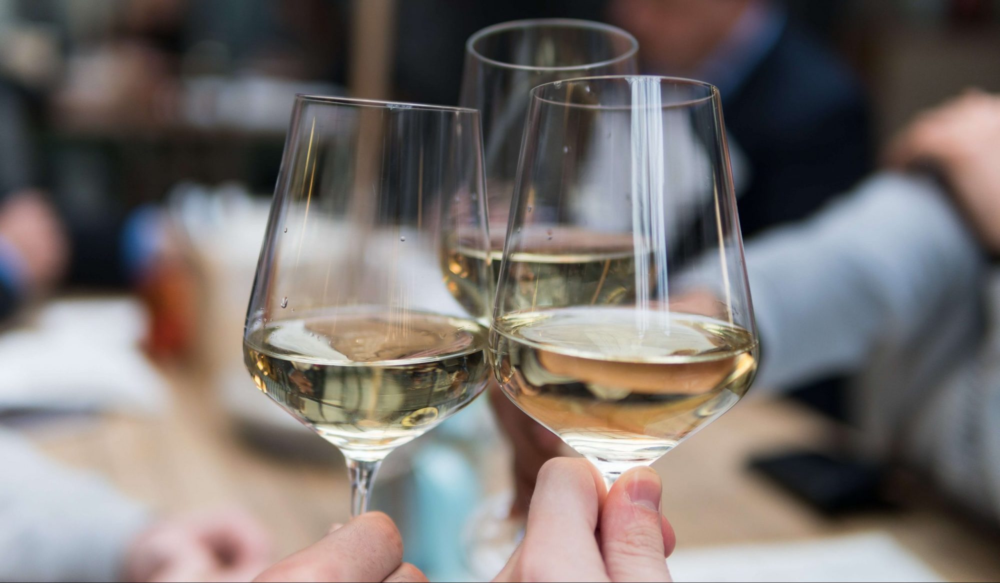 Tres copas de vino blanco sujetadas por manos